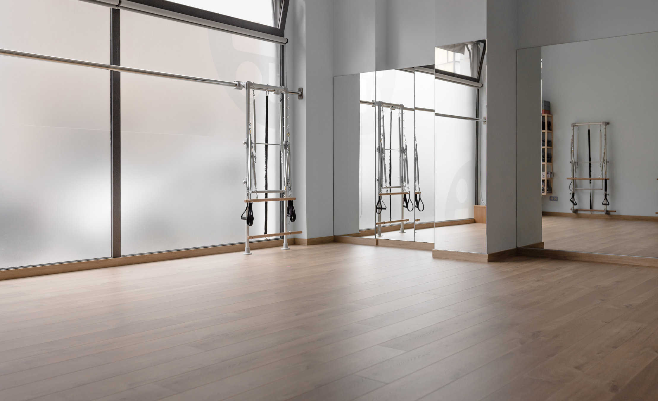 pilates studio corner where you can see a wooden floor, a large window, a mirror and a pilates machine