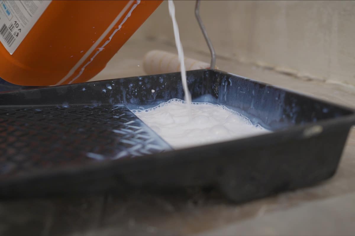 A worker pours a primer from an orange canister.. Worker pouring a primer in a paint tray